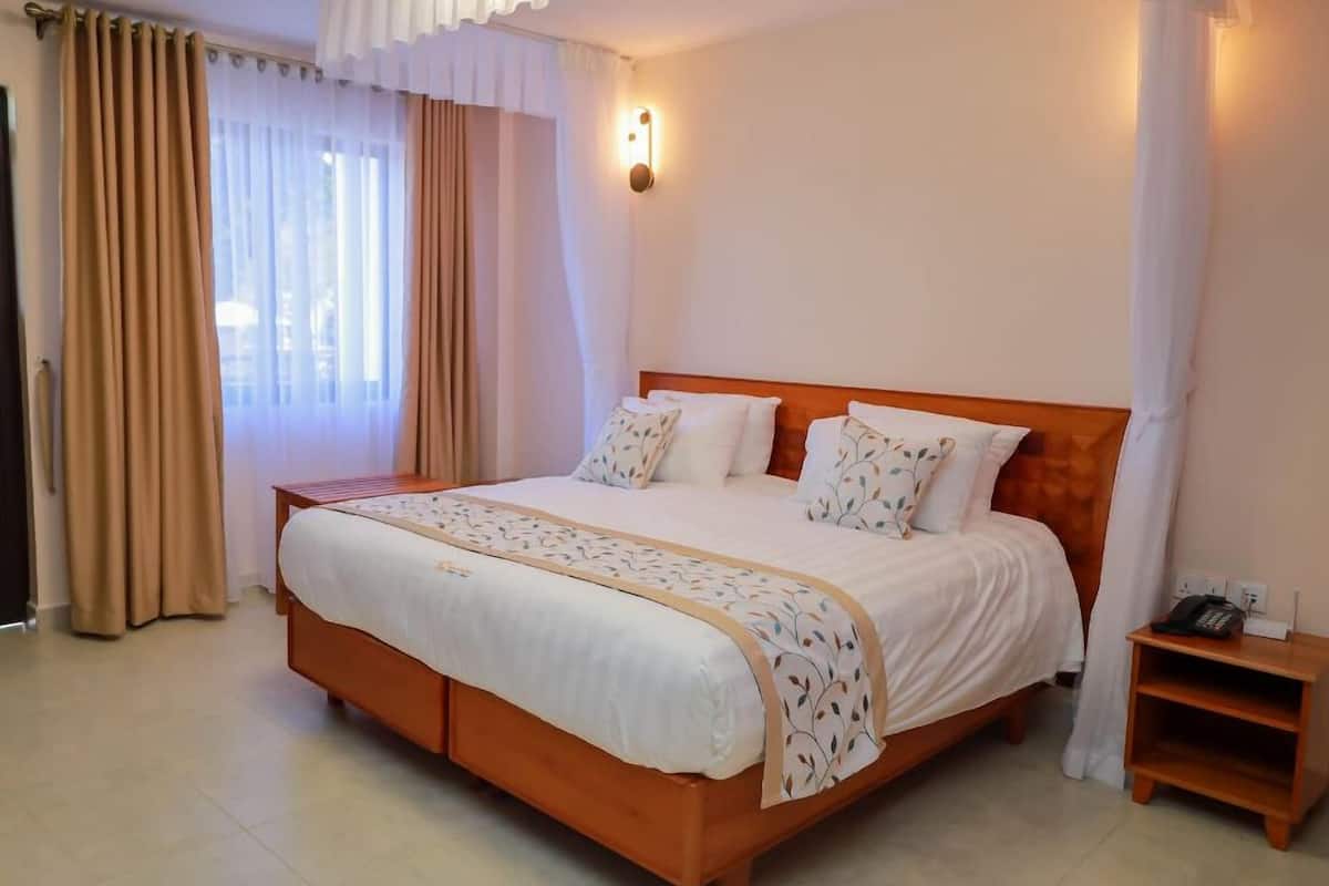Une chambre d’hôtel avec un grand lit, une table de chevet et une fenêtre avec des rideaux.