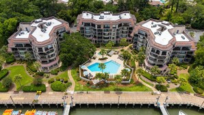 Un moderno complejo de apartamentos con una piscina central, rodeado de abundante vegetación y un muelle con barcos.
