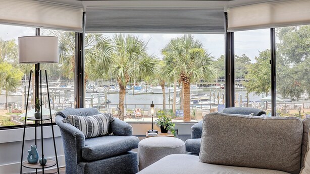 Una habitación de esquina con ventanas amplias, un sofá, una silla y una lámpara.