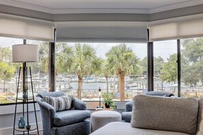 Ein Eckzimmer mit großen Fenstern, einem Sofa, einem Sessel und einer Lampe.