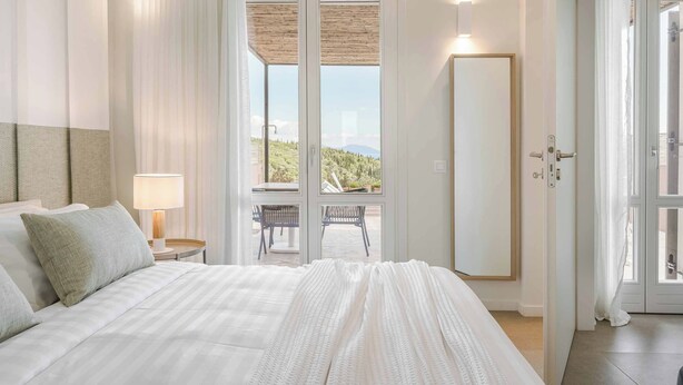Een hotelkamer met een groot bed, een zithoek met uitzicht en een balkon met tafel en stoelen.