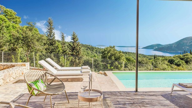 Area piscina con sedie a sdraio, un tavolo e vista su un lago e montagne.