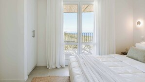 Una camera da letto con un letto grande, tende bianche e vista su un balcone con ringhiera.