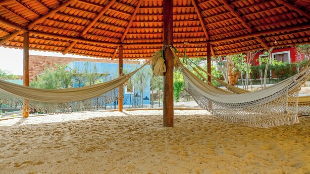 A hammock under a tiled roof, a sandy ground, and a building with a blue wall in the background.
