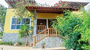 A yellow building with a stone facade, wooden staircase, and a wooden pergola with pink flowers.