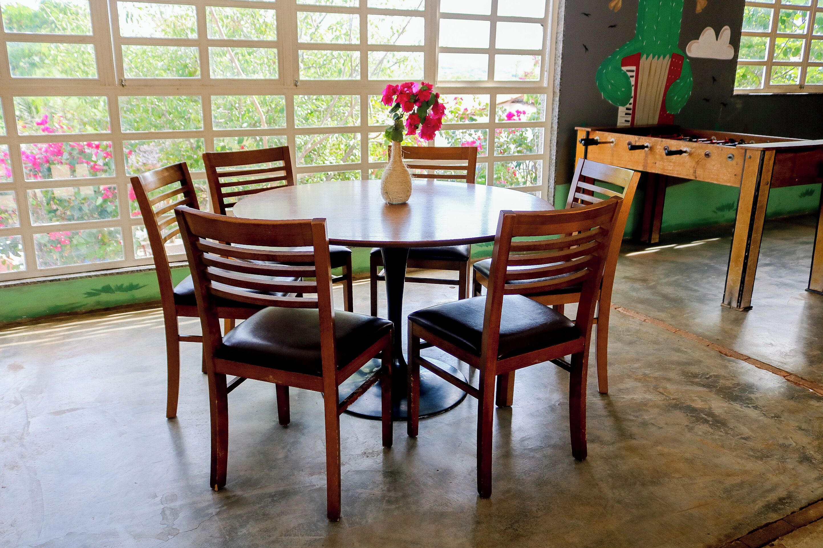 Een ronde houten tafel met vier stoelen, een vaas met bloemen en een tafelvoetbal in de achtergrond.