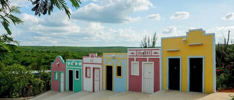 A row of colorful buildings with doors and windows, set against a backdrop of greenery and a clear sky.