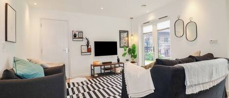 Un salon moderne avec un sol à carreaux noirs et blancs, un téléviseur à écran plat et deux canapés.