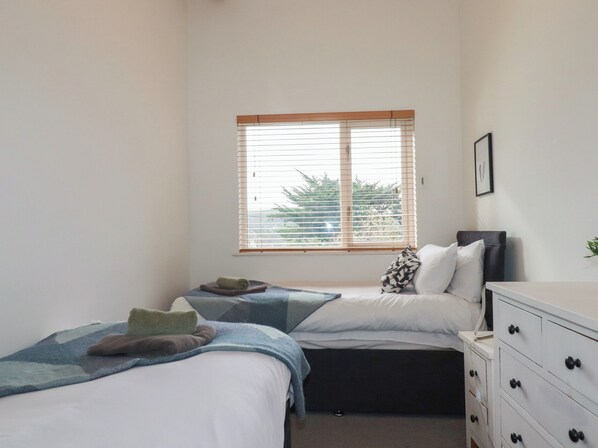 A bedroom with two beds, a window with blinds, a dresser with drawers, and a framed picture on the wall.