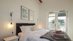 A bedroom with a bed, bedside table, and a window with a view of greenery. - Treveglos (Truro)