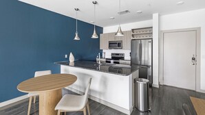 A modern kitchen with a blue accent wall, stainless steel appliances, and a central island with seating. - Landing | Modern 1BD, Gym, Pool (McKinney)