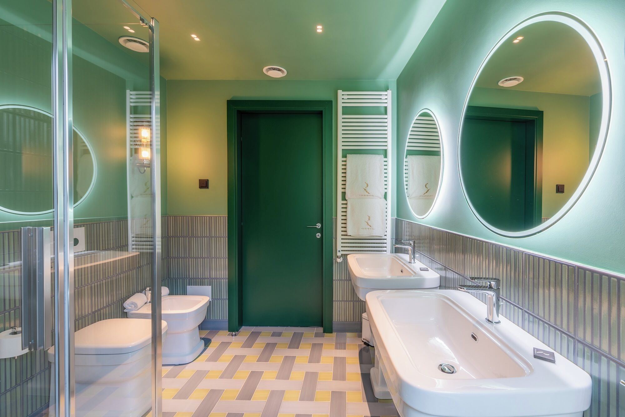 Un baño moderno con una puerta verde, dos lavamanos, un inodoro y una zona de ducha.