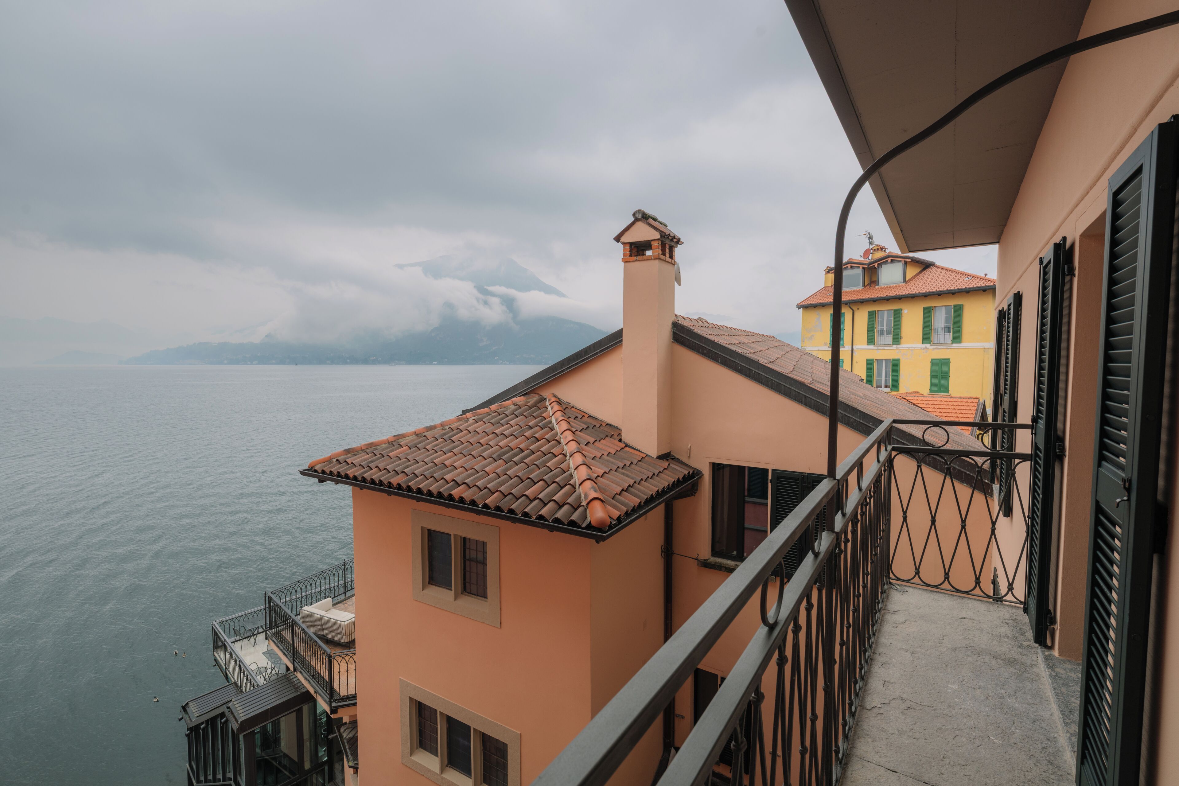 Ein Balkon mit Blick auf das Meer und die Berge, ein Gebäude mit Ziegeldach und Geländer.