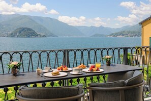 A dining table with plates of food, cups, and a vase of flowers, overlooking a lake with mountains in the background. - Casa Du Lac - by R Collection Hotels (Varenna)