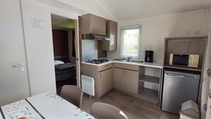 Eine kompakte Küchenzeile mit Herd, Spüle und Mikrowelle. Im Hintergrund ist ein Bett zu sehen.
