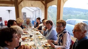 Een groep mensen zit aan een lange tafel met borden eten en glazen, onder een tent met uitzicht op de natuur.