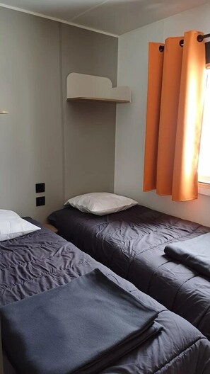 Une chambre avec deux lits, un mur blanc et des rideaux orange.