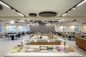 A spacious cafeteria with multiple tables and a central buffet area.