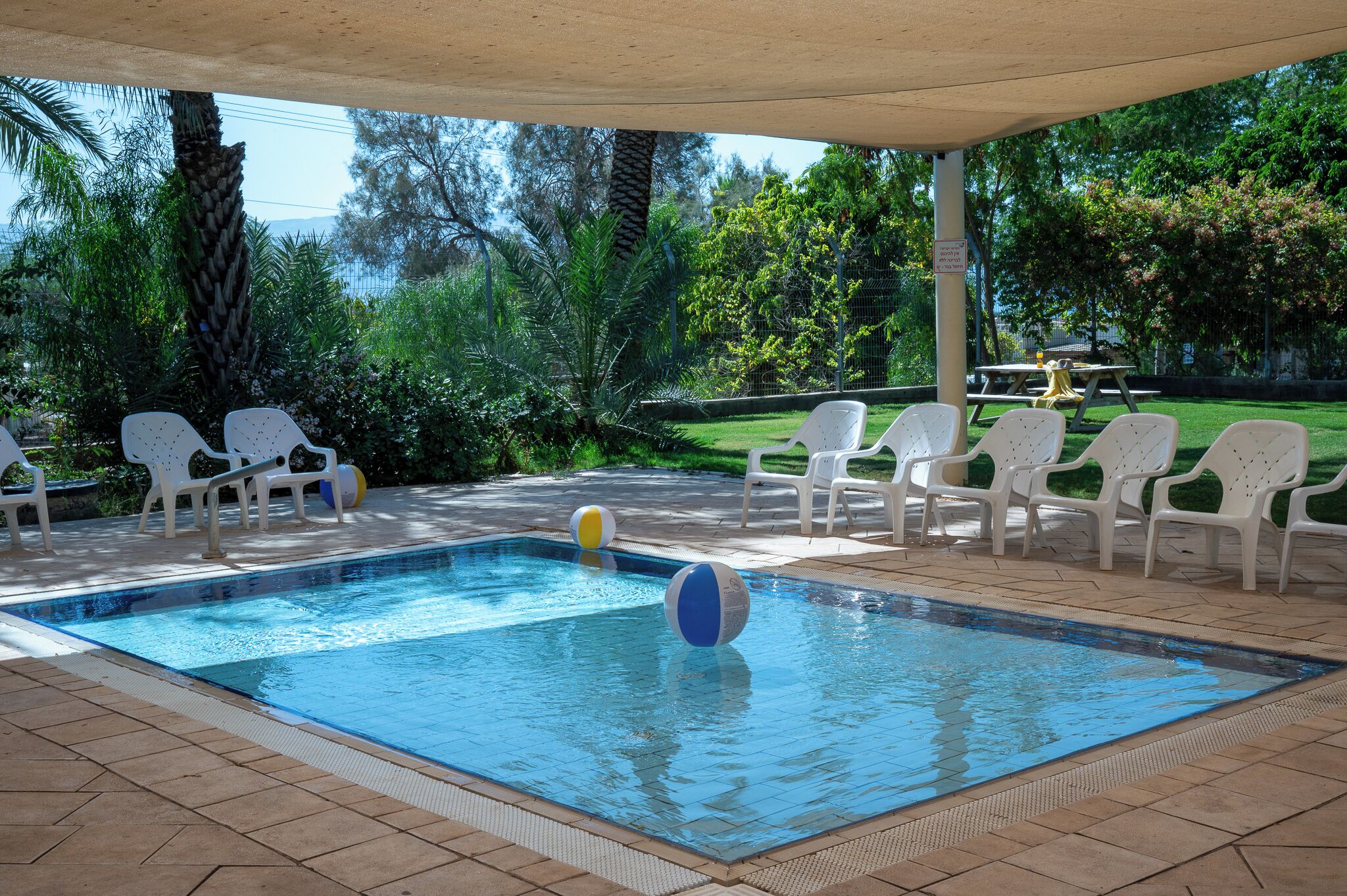 A swimming pool with white chairs and a covered area.