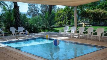 A swimming pool with white chairs and a covered area.