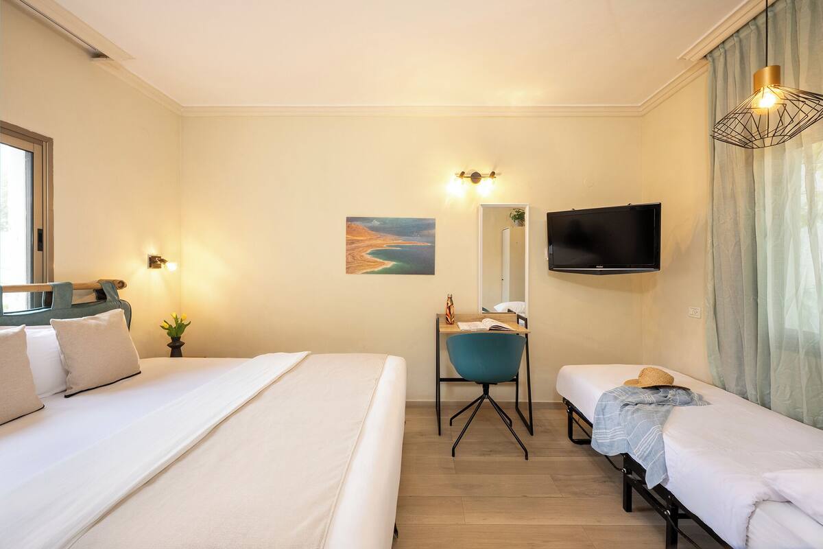 Ein Hotelzimmer mit zwei Betten, einem Schreibtisch, einem Stuhl, einem Fernseher und einem Bild an der Wand.