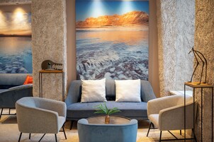 A modern lobby with a sofa, armchairs, a coffee table, and a large wall mural of a desert landscape.