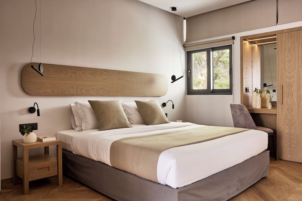 A modern bedroom with a large bed, bedside tables, a desk, and a window with a view of trees.