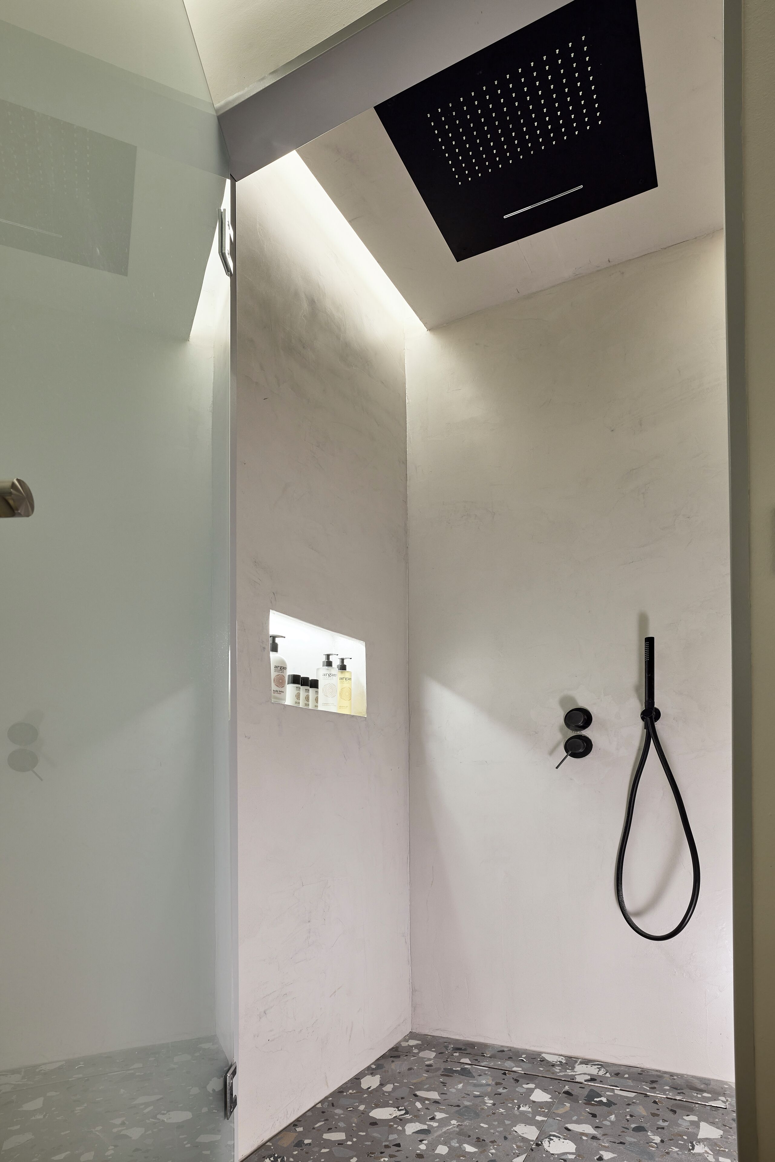 Eine moderne Dusche mit Bedienfeld, Handbrause und Fliesenboden.