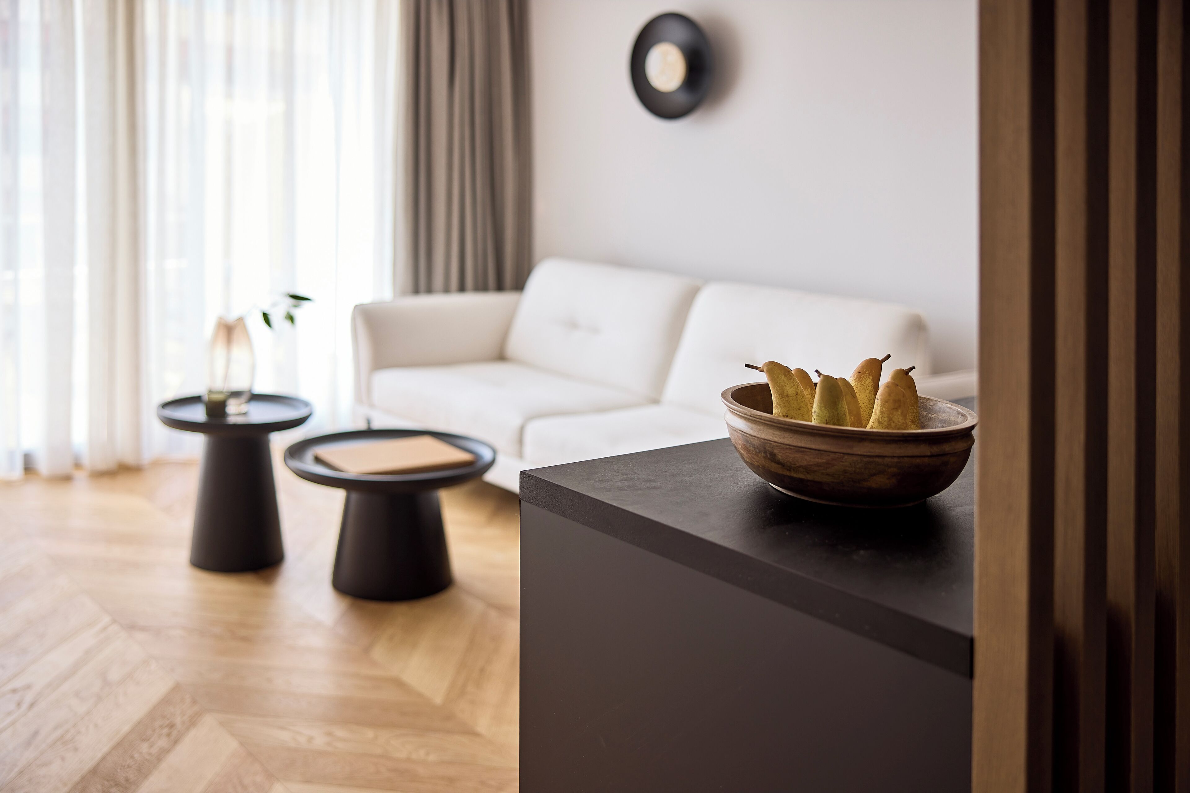 A modern living room with a white sofa, two black side tables, and a wooden bowl on a dark surface.
