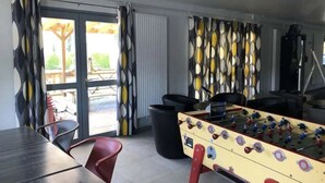 Een kamer met een tafelvoetbaltafel, een eettafel en een groot raam met gordijnen.