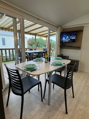 A dining area with a table set for four, chairs, a television mounted on the wall, and a view of the outdoors.
