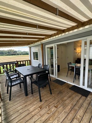A covered patio with a table and chairs, a sliding glass door leading to an interior dining area, and a view of a field.