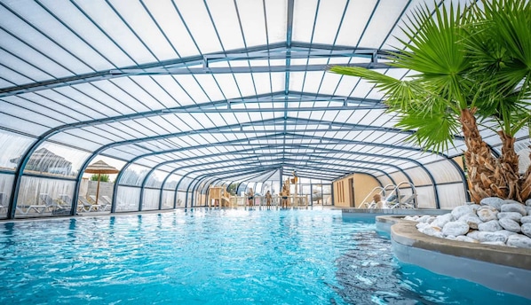 An indoor swimming pool with a glass ceiling and palm trees. - ZEcamping parc aquatique pet friendly club enfant (Saint-Jean-de-Monts)