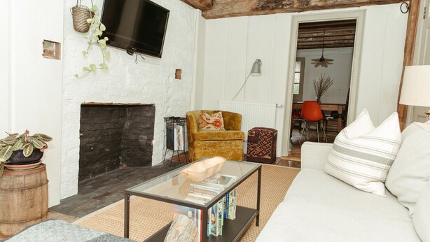 A living room with a fireplace, a sofa, a coffee table, a TV, and a door leading to another room.