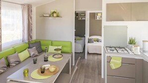 A compact living space with a green sofa, a dining table with a bowl of food, a kitchen area with a stove, and a small seating area with a white sofa.