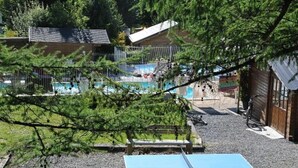 Ein Poolbereich mit Tischtennisplatte, einem umzäunten Schwimmbecken und einem Gebäude mit Satteldach.