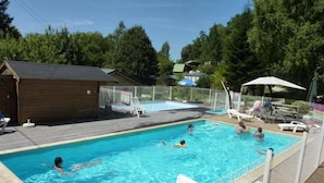 Ein Schwimmbecken mit mehreren Bahnen, umzäumt von einem Zaun, ausgestattet mit Liegestühlen und Sonnenschirmen.