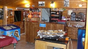 A restaurant interior with a wooden ceiling, a bar area with bottles, a counter with a sign, and a table with a box of ice cream.