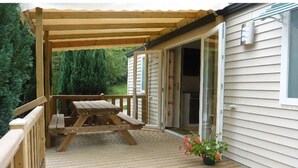 A wooden deck with a picnic table, a covered area, and a house with a sliding glass door.