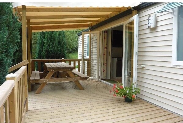 A wooden deck with a picnic table, a covered area, and a house with a sliding glass door.