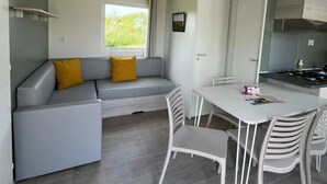 Ett modernt kök med en matplats, en grå soffa med gula kuddar och ett fönster med utsikt över grönområden.