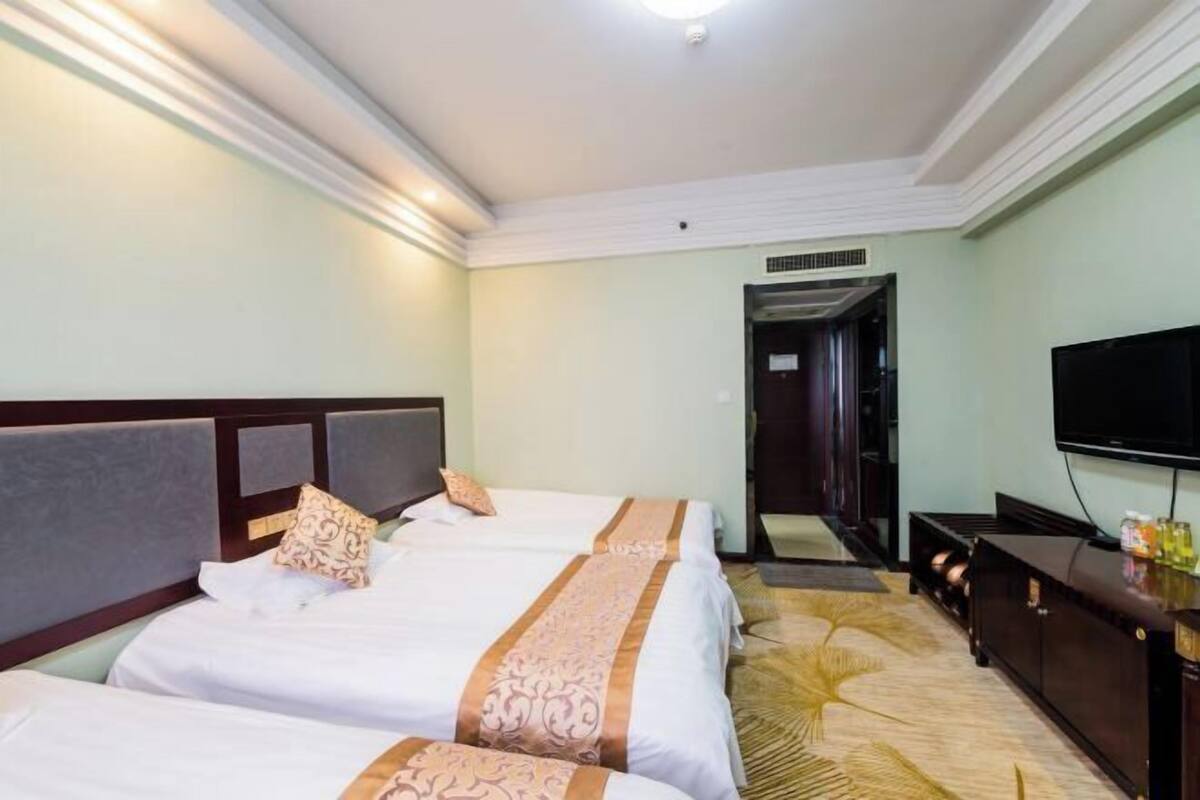 Une chambre d’hôtel avec deux lits, une télévision, un minibar et un sol recouvert de moquette.