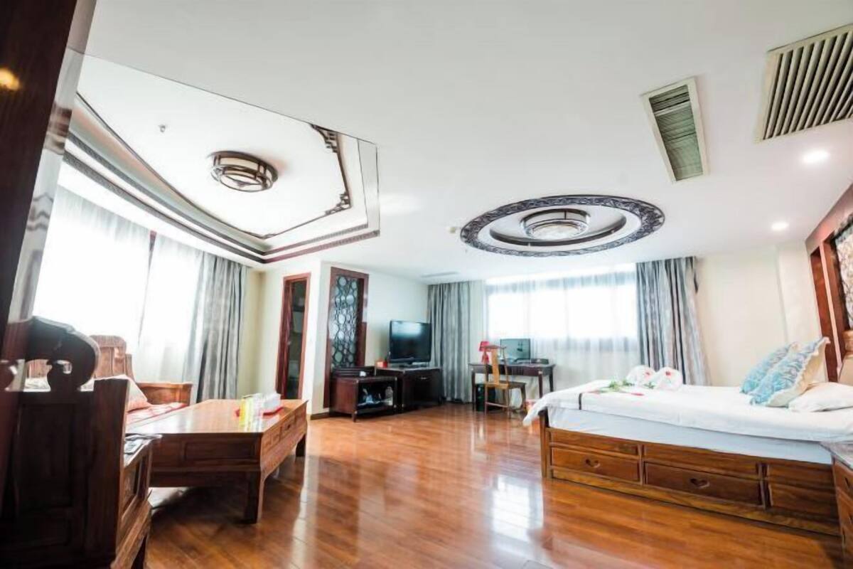 Une chambre d’hôtel avec un plancher en bois, un lit, un bureau, une télévision et une fenêtre avec des rideaux.