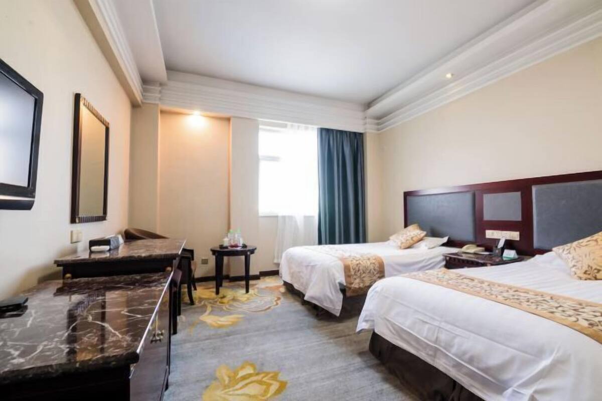 Une chambre d’hôtel avec deux lits, un bureau, une chaise, une petite table et un grand miroir.