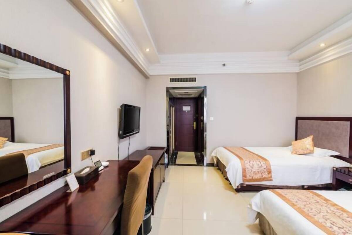 Une chambre d’hôtel équipée d’un bureau, de deux lits, d’une télévision et d’un miroir.