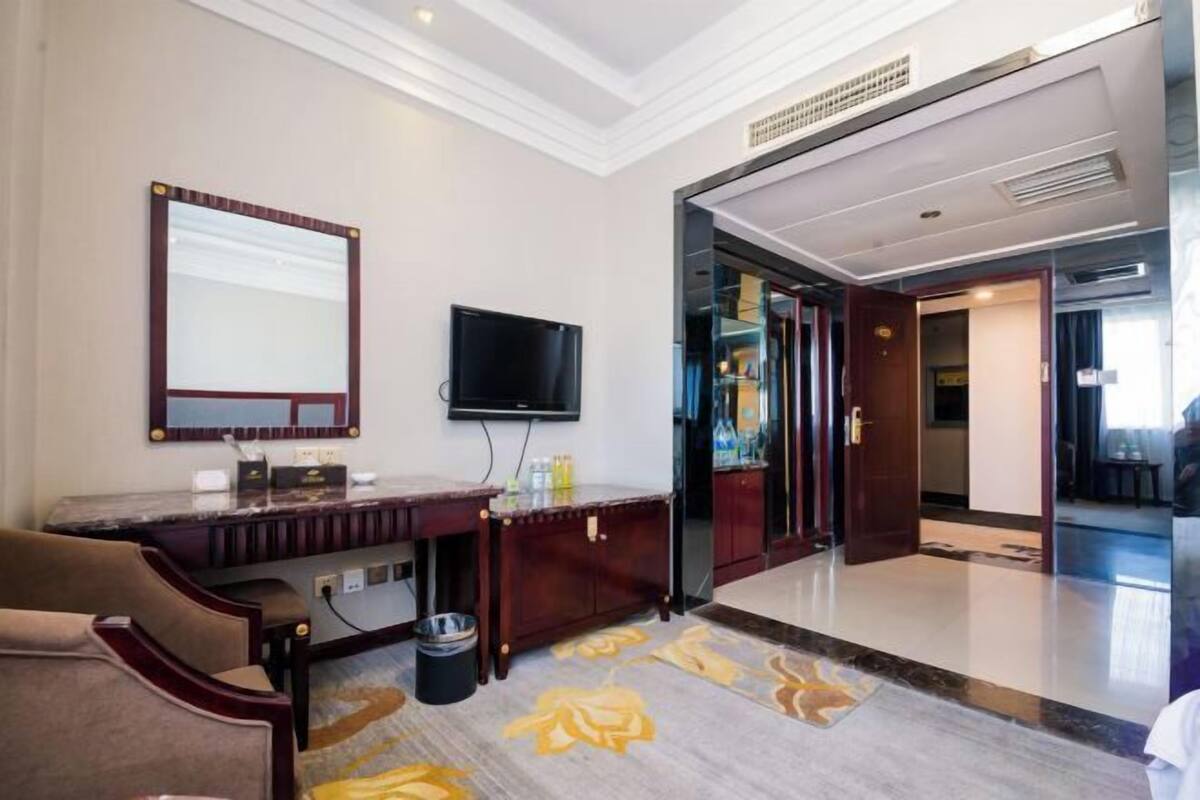 Une chambre d’hôtel dotée d’un grand miroir, d’un téléviseur à écran plat, d’une coiffeuse avec miroir, d’un bureau et d’une chaise.