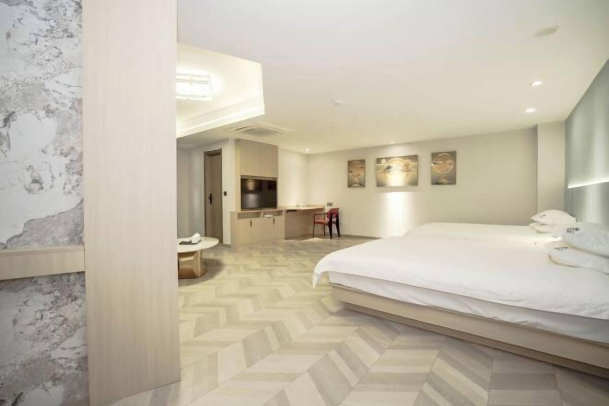 Une chambre d’hôtel moderne avec un grand lit, un petit bureau et un parquet à motifs en chevrons.
