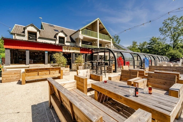 An outdoor seating area with wooden benches and tables, a covered patio, and a building with a green roof and a red awning.