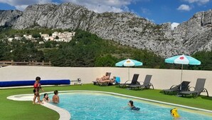 Une piscine avec des personnes, des chaises longues et des parasols.