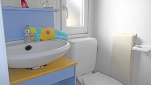 Une salle de bain avec un lavabo blanc, un meuble bleu et jaune, et des toilettes blanches.